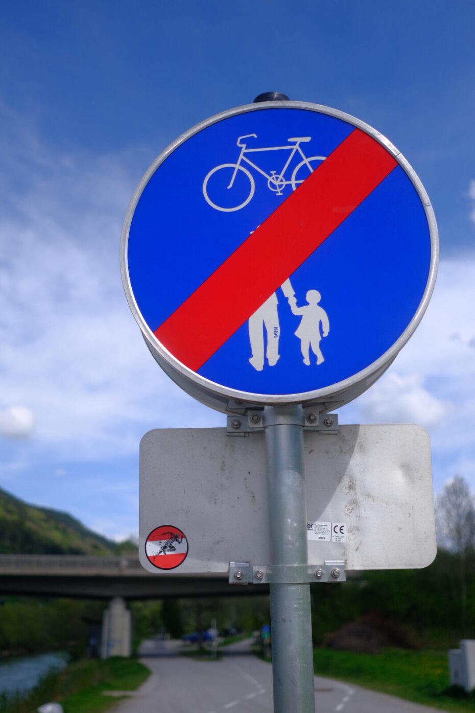 Schild, das das Ende eines gemeinsam Fuß- und Radweges markiert, ein Aufkleber mit den österreichischen Nationalfarben und einem stilisierten Läufer klebt auf der Rückseite des darunter angebrachten Schilds