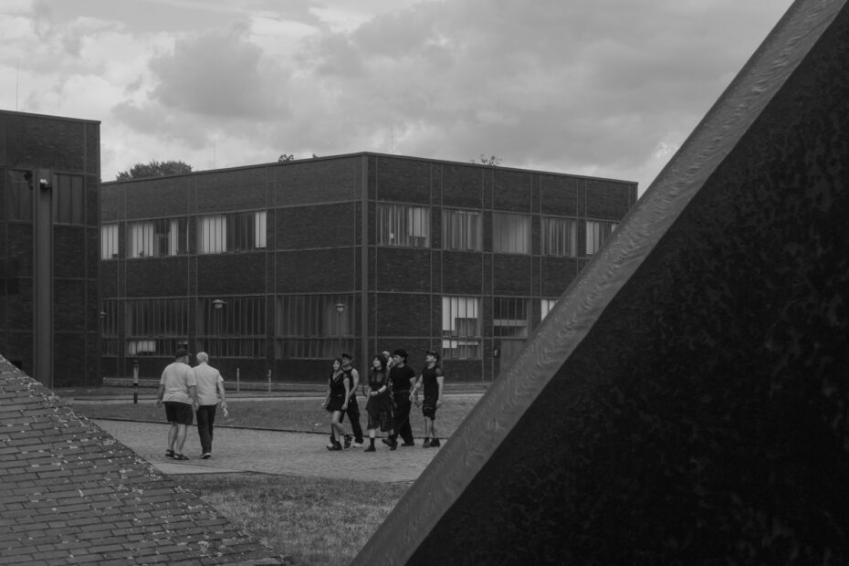 Schwarz-Weiß Bild, das Menschen auf dem Weg zum Festival zeigt, zwei Gruppen laufen hierbei aufeinander zu, die einen hell, die anderen dunkel gekleidet