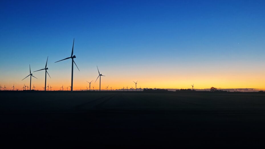 Sonnenaufgang über Nordfriesland, der Horizont färbt sich von einem dunklen blau zu einem Gold und Orange. Die Schatten von Windräder sind zu sehen